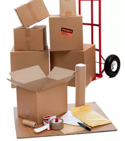 A variety of packing supplies are neatly arranged on a shelf. Cardboard boxes of various sizes are stacked alongside rolls of packing tape, bubble wrap, and other protective materials.